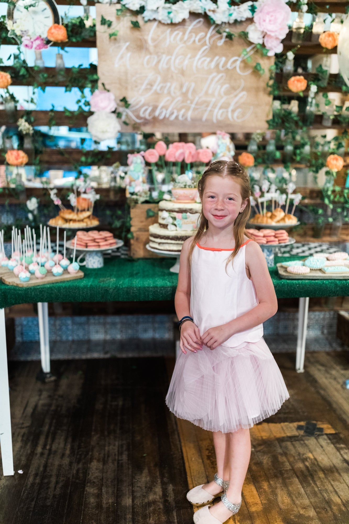 birthday girl standing in front of an Alice in Wonderland themed sweet treat table at her birthday party