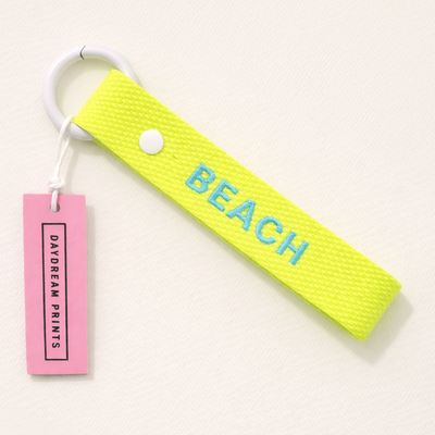 Neon green keychain with 'BEACH' text and pink tag on a white background