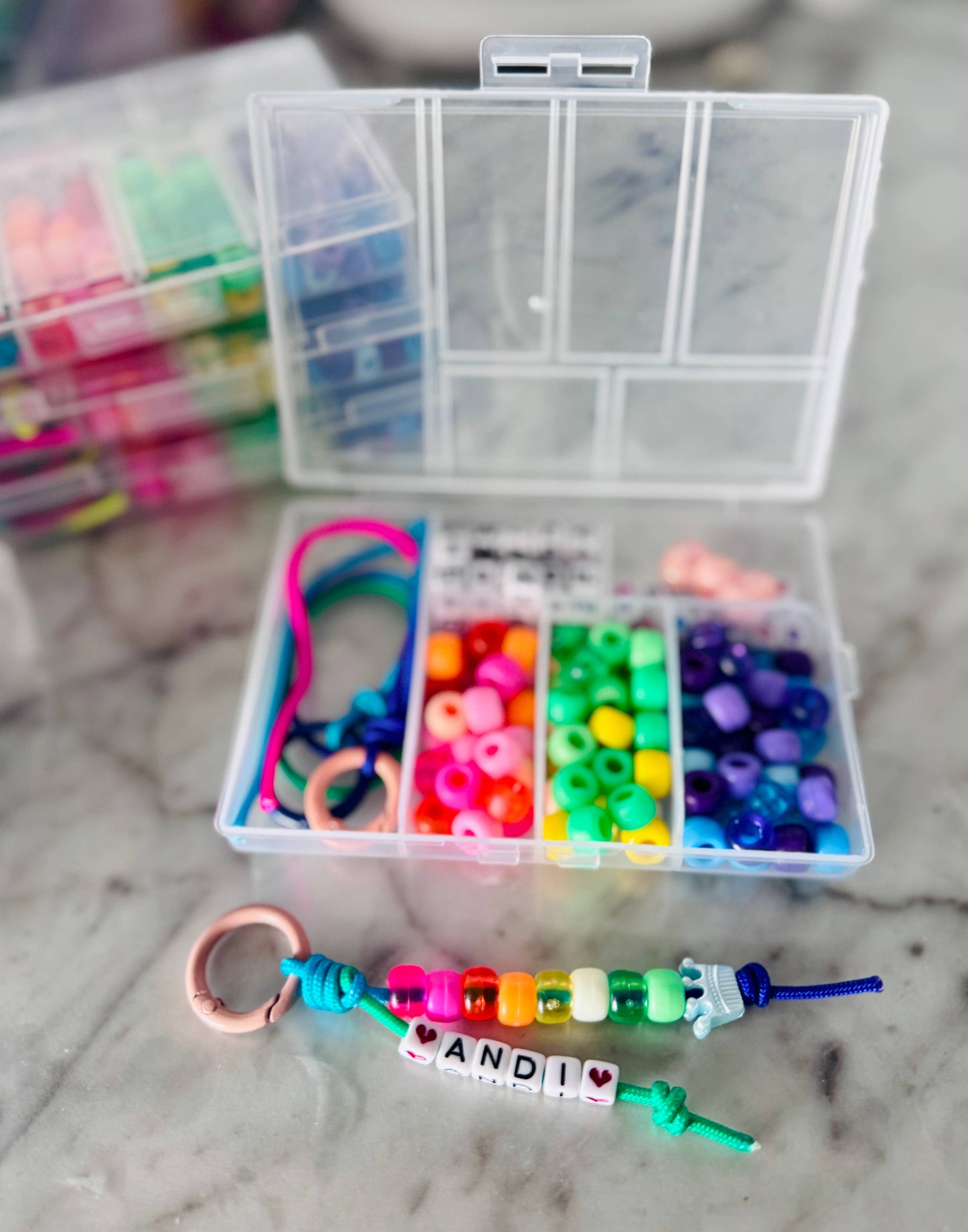 Clear plastic jewelry-making kit with beads and a bracelet on a marble surface