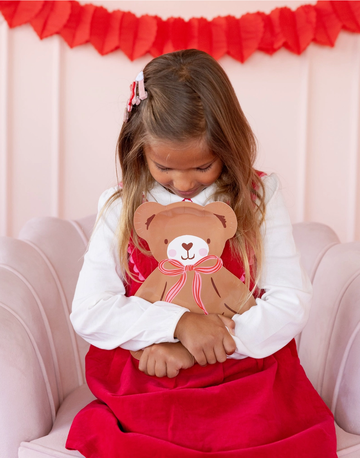 Young girl holding a teddy bear in front of a red decorative background