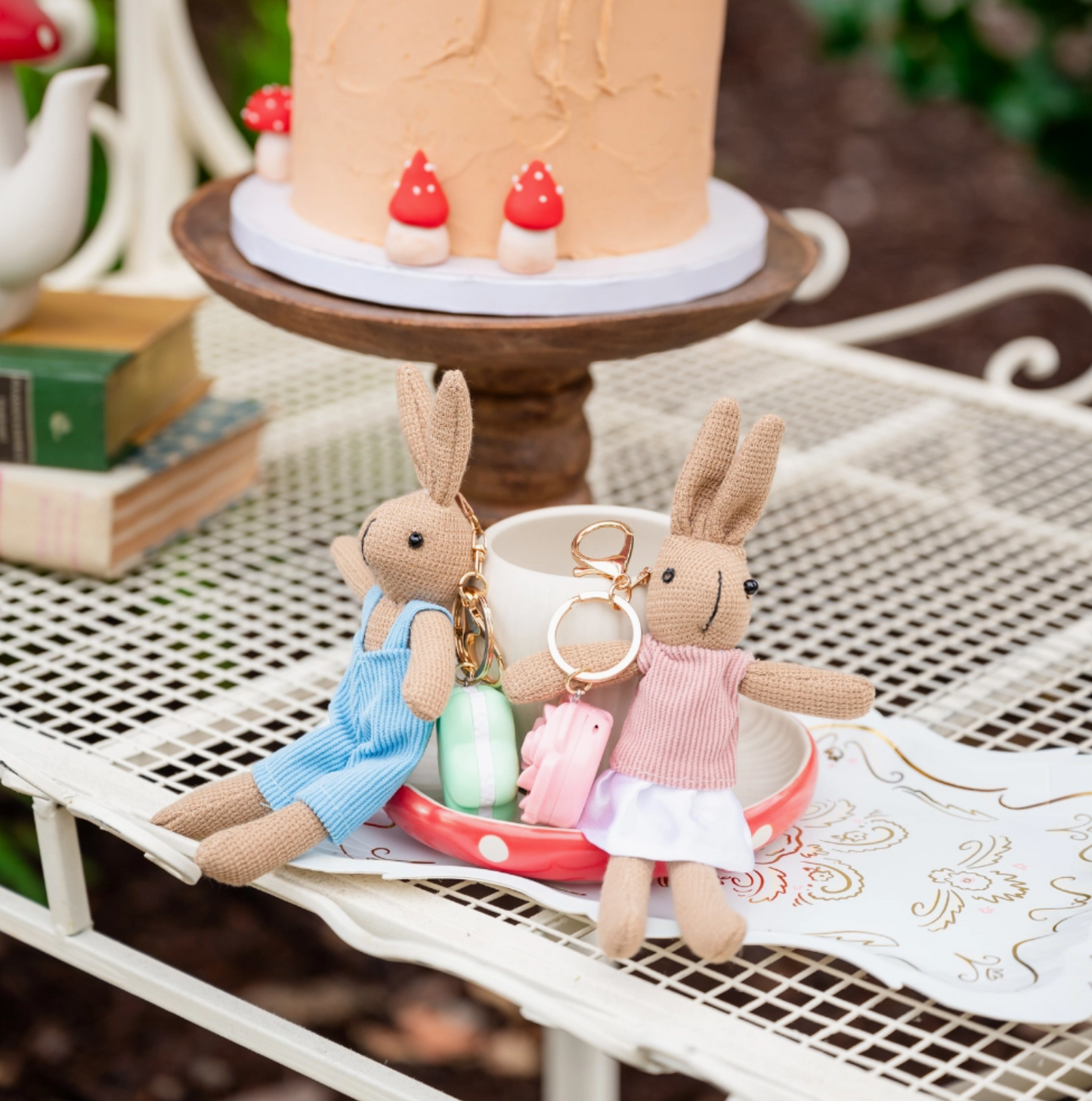 Two plush rabbit toys with keychains on a table with a cake in the background.