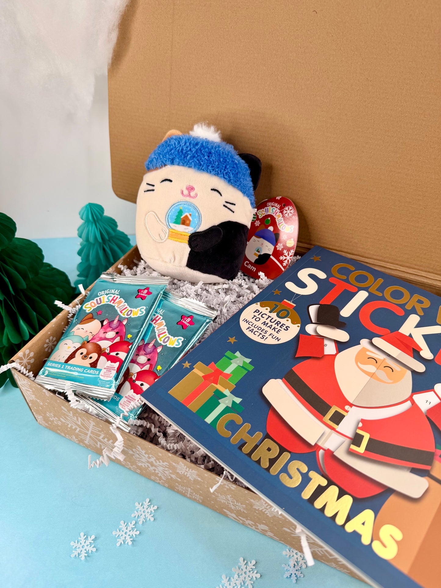 Gift box with a plush toy, books, and a 'Color Stick Christmas' book on a light blue surface.