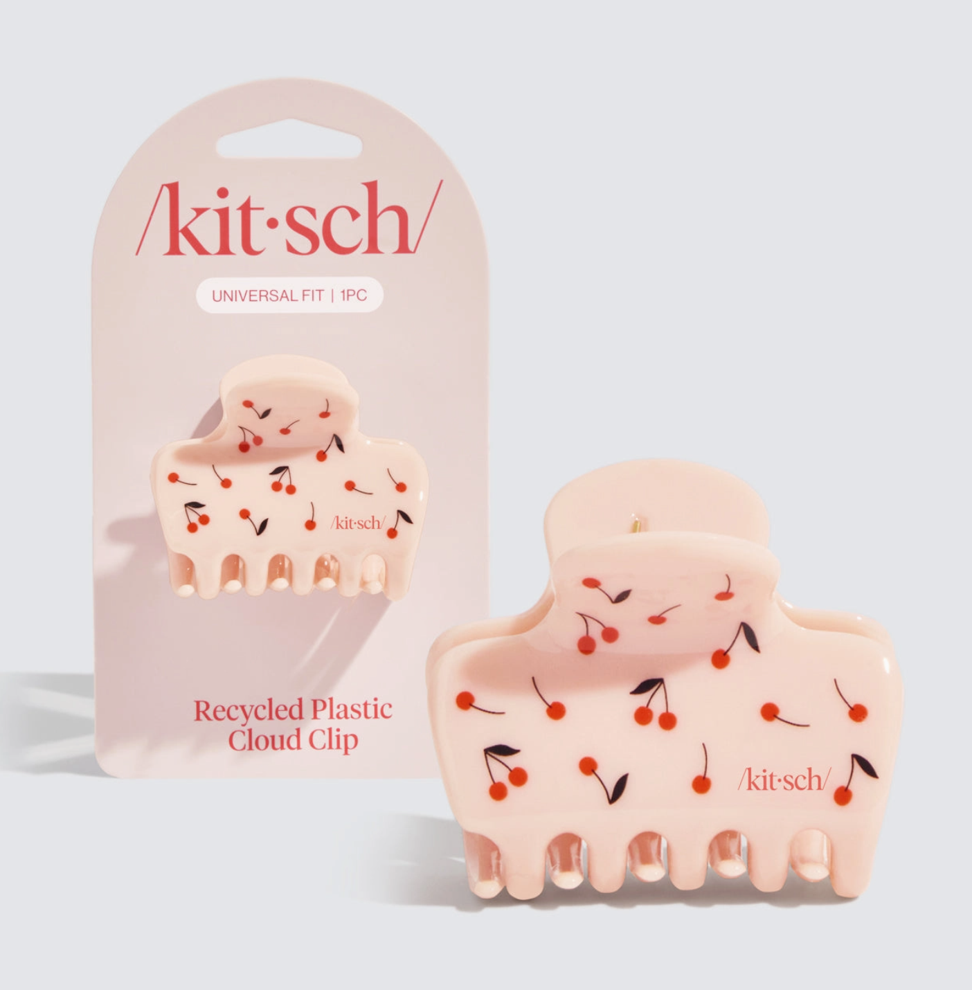 A medium-sized hair clip with a cherry print design, made from recycled plastic, packaged in a clear plastic packaging with the brand name 'kitsch' visible.