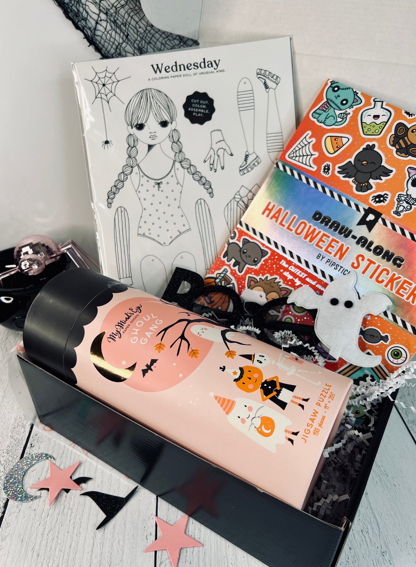 A gift box with various Halloween-themed items including a sticker book, a puzzle, glasses, and a coloring sheet, wrapped with a ribbon and tagged with 'Creative Wednesday'.