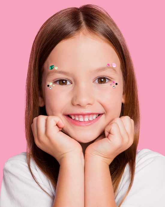Young girl with decorative stickers on her face against a pink background