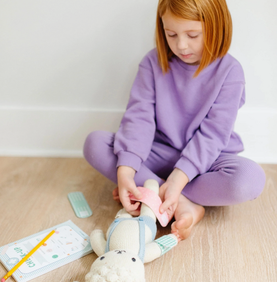 Child in purple outfit playing with a plush toy on a wooden floor.