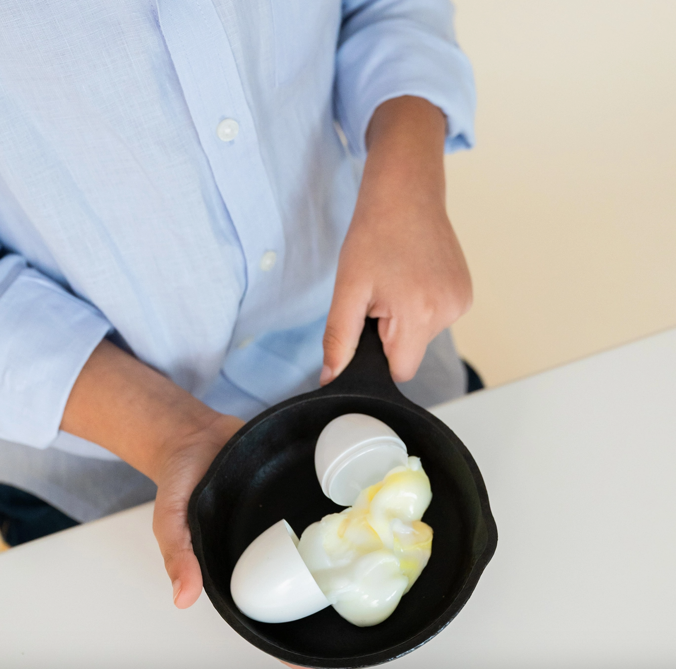 Person holding a small black frying pan with two white bottles inside on a light surface.