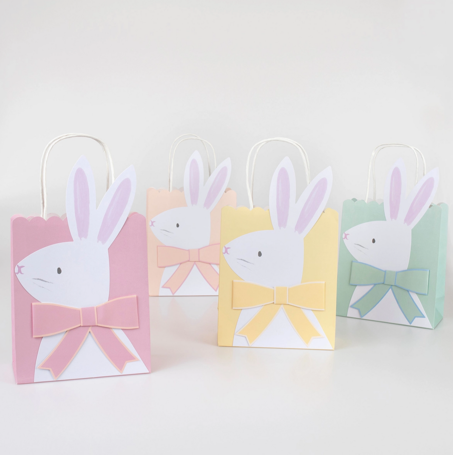 Four pastel-colored gift bags with bunny designs on a white background