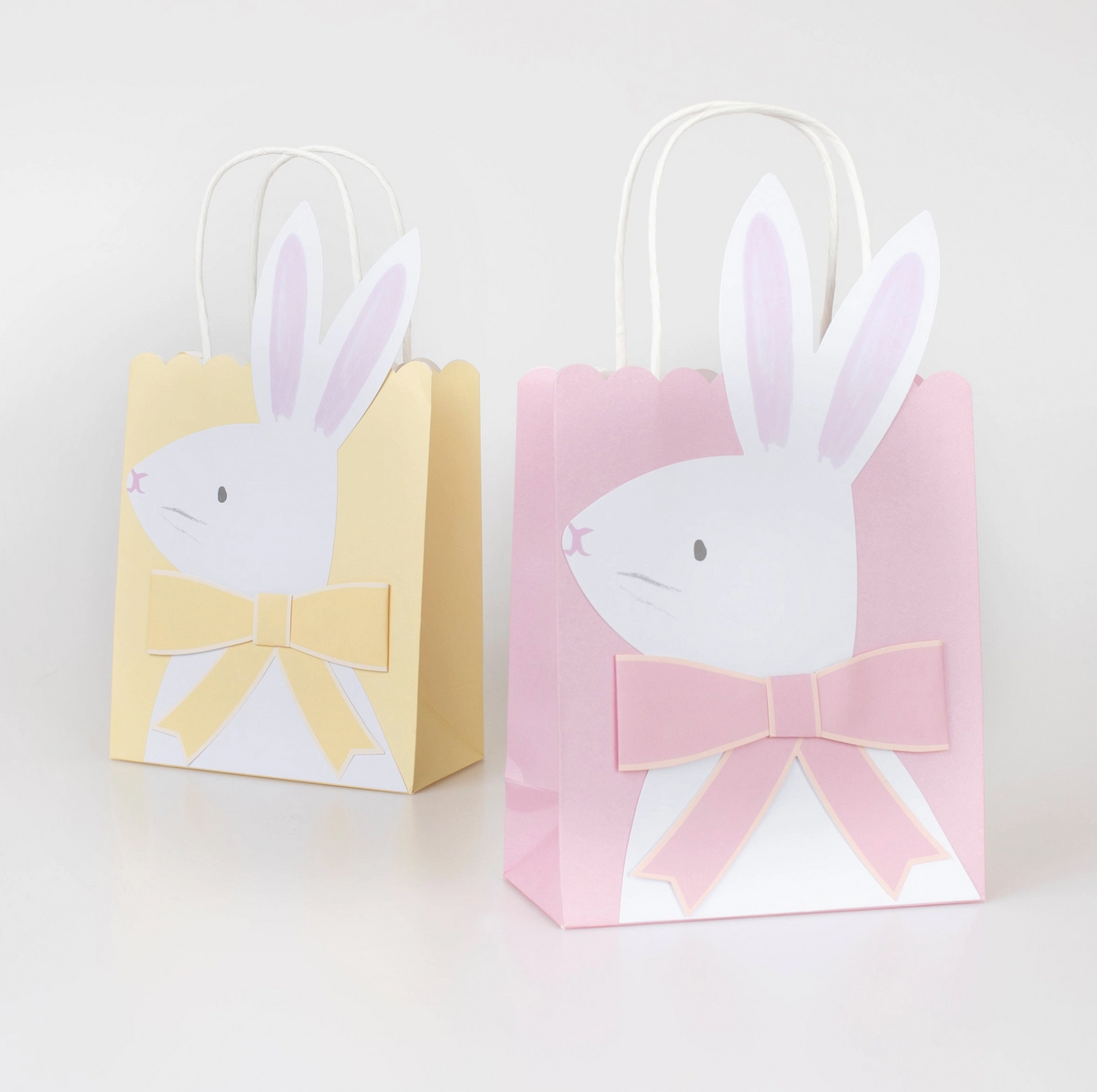Two paper gift bags with bunny faces and bows on a white background