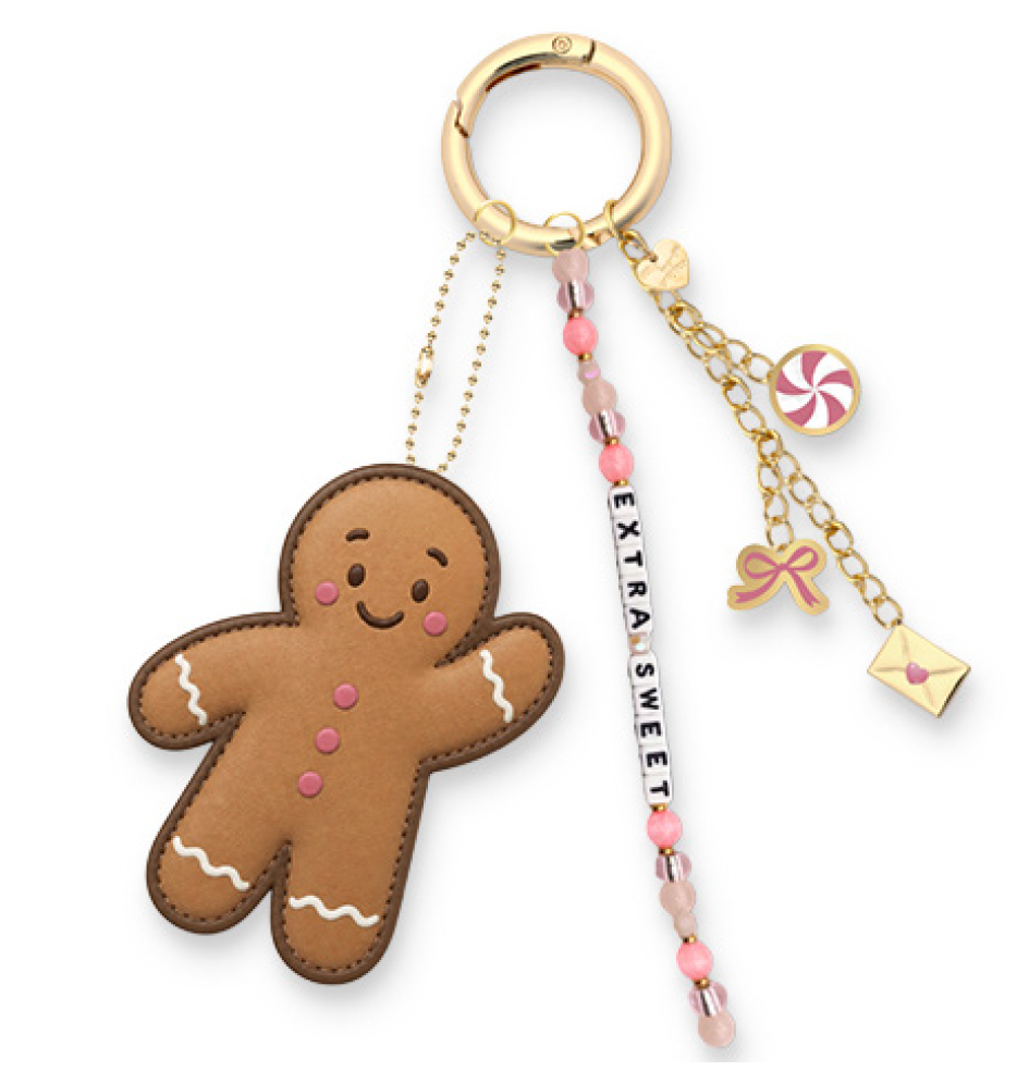 A gingerbread man keychain charm with a gold-tone ring, pink and white bead chain, and multiple dangling charms including a candy, bow, envelope, and a white bead with the text 'EXTRASWEET'.