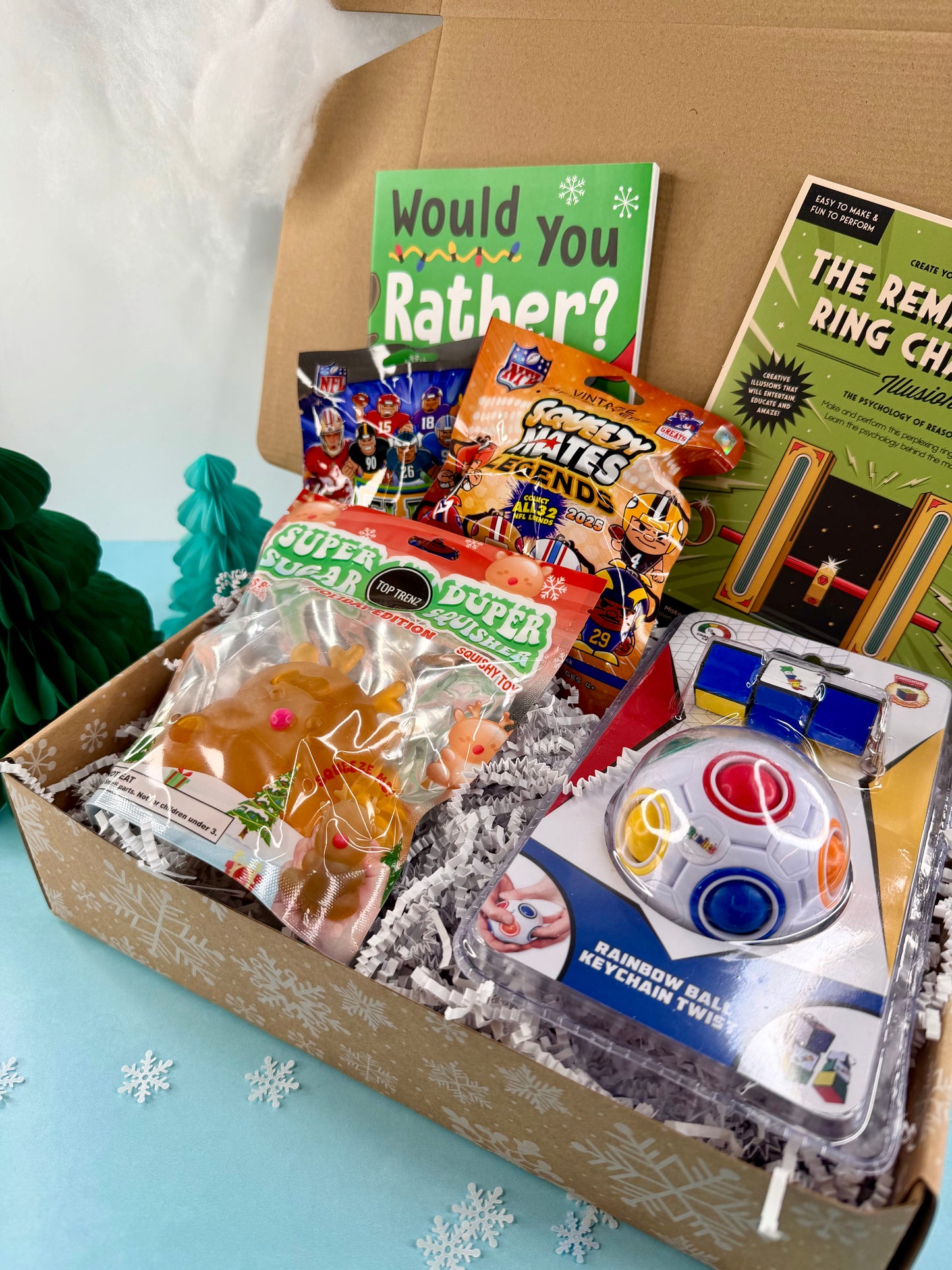 Box of children's toys and games with 'Would You Rather?' card on a light blue background