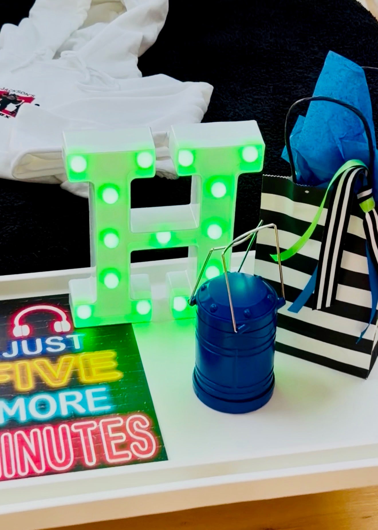 Decorative letter 'H' with green lights, blue container, and colorful sign on a surface.