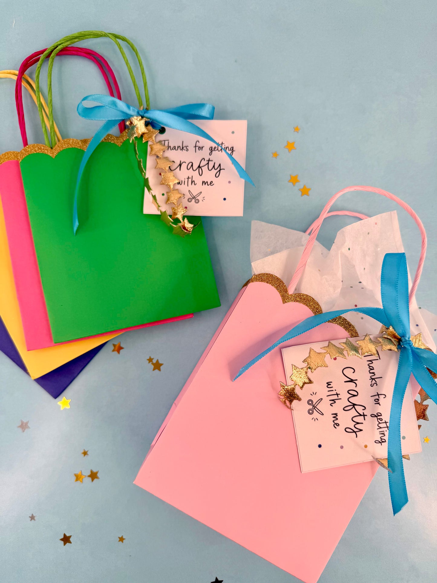 Colorful gift bags with ribbons and 'Thanks for getting crafty with me' tags on a light blue background.
