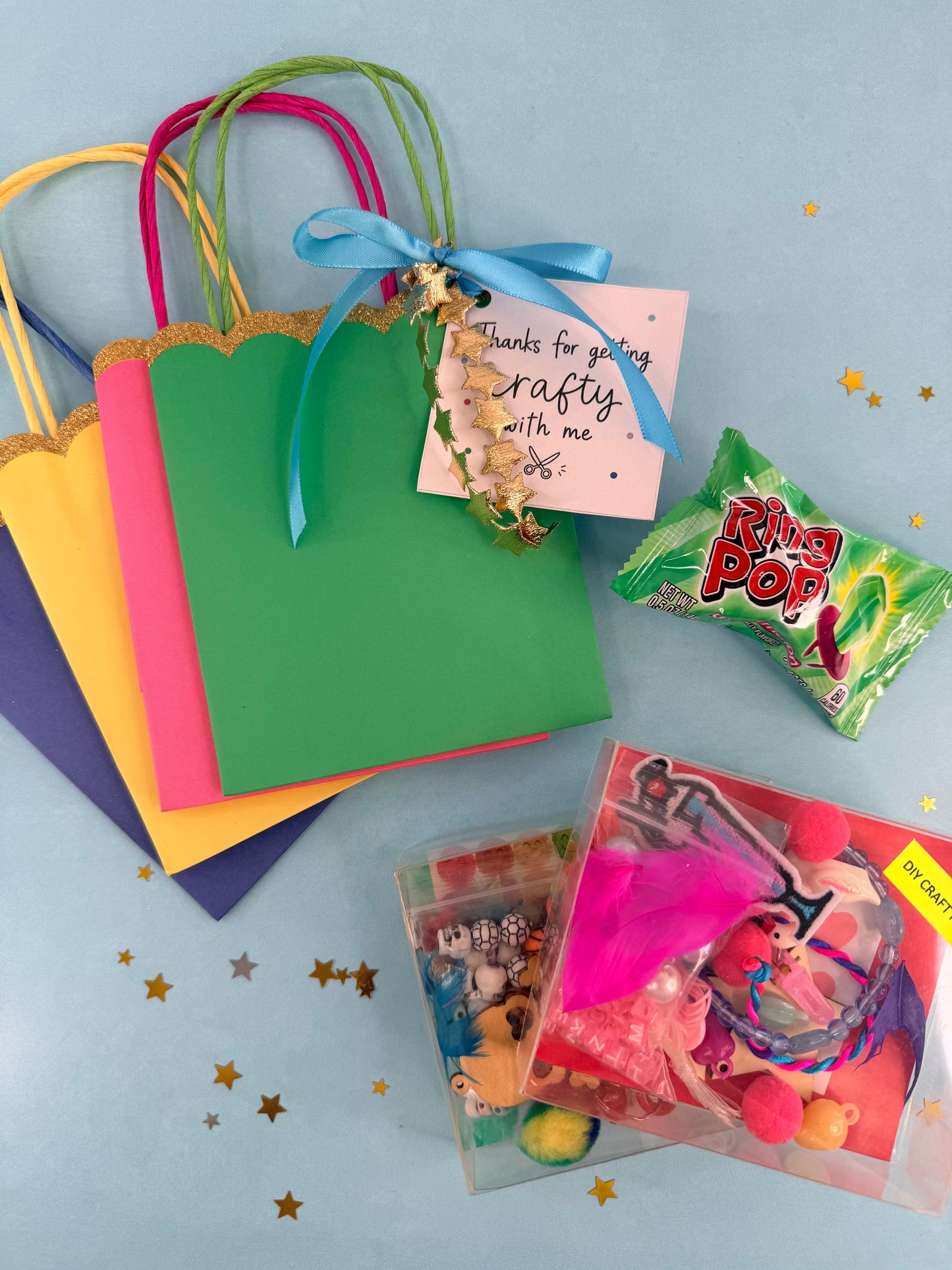 Colorful gift bags with a 'Thanks for getting crafty with me' tag, Rolo candy, and vintage-style toys on a light blue background.