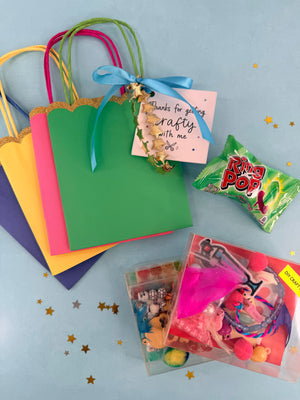 Colorful gift bags with a 'Thanks for getting crafty with me' tag, Rolo candy, and vintage-style toys on a light blue background.