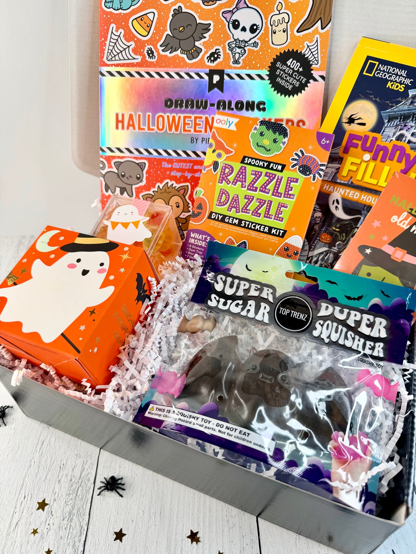 Open Halloween gift box with sticker activities, a gem sticker kit, a haunted house activity book, candy, and Halloween squishy toys.