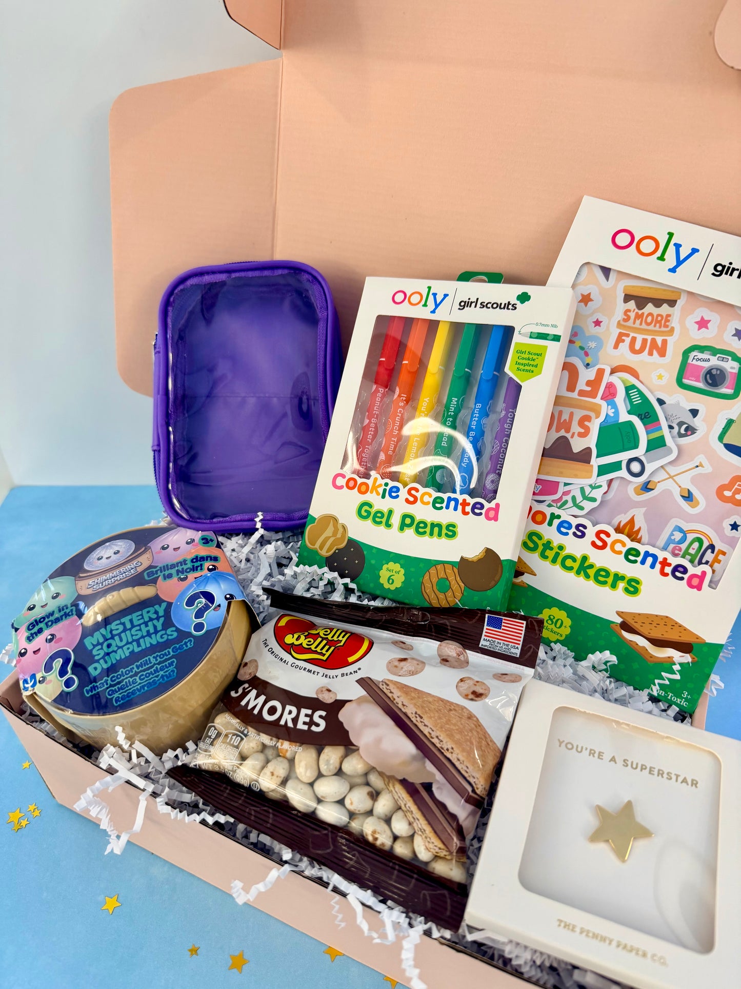 Personalized Girl Scout celebration gift box for kids with cookie-scented gel pens, stickers, s’mores candy, a purple pouch, and creative surprises.