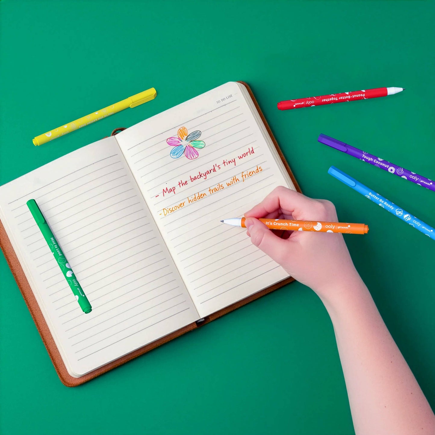 Hand writing in a notebook with colorful pens on a green background