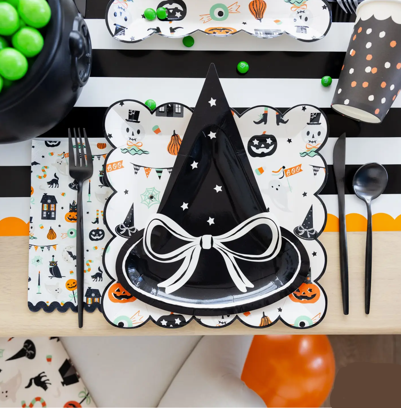Halloween-themed table setting with witch hat plate, black and white striped placemat, and colorful decorations.