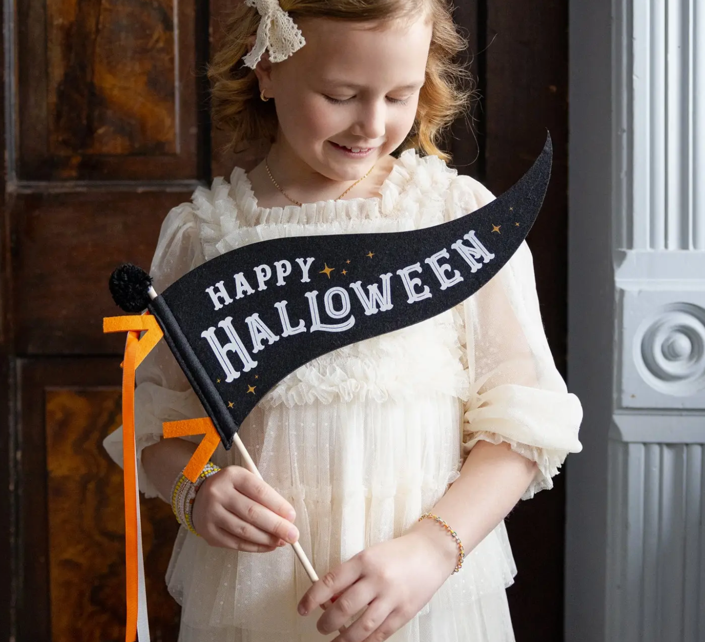 Young girl holding a 'Happy Halloween' sign in front of a door.