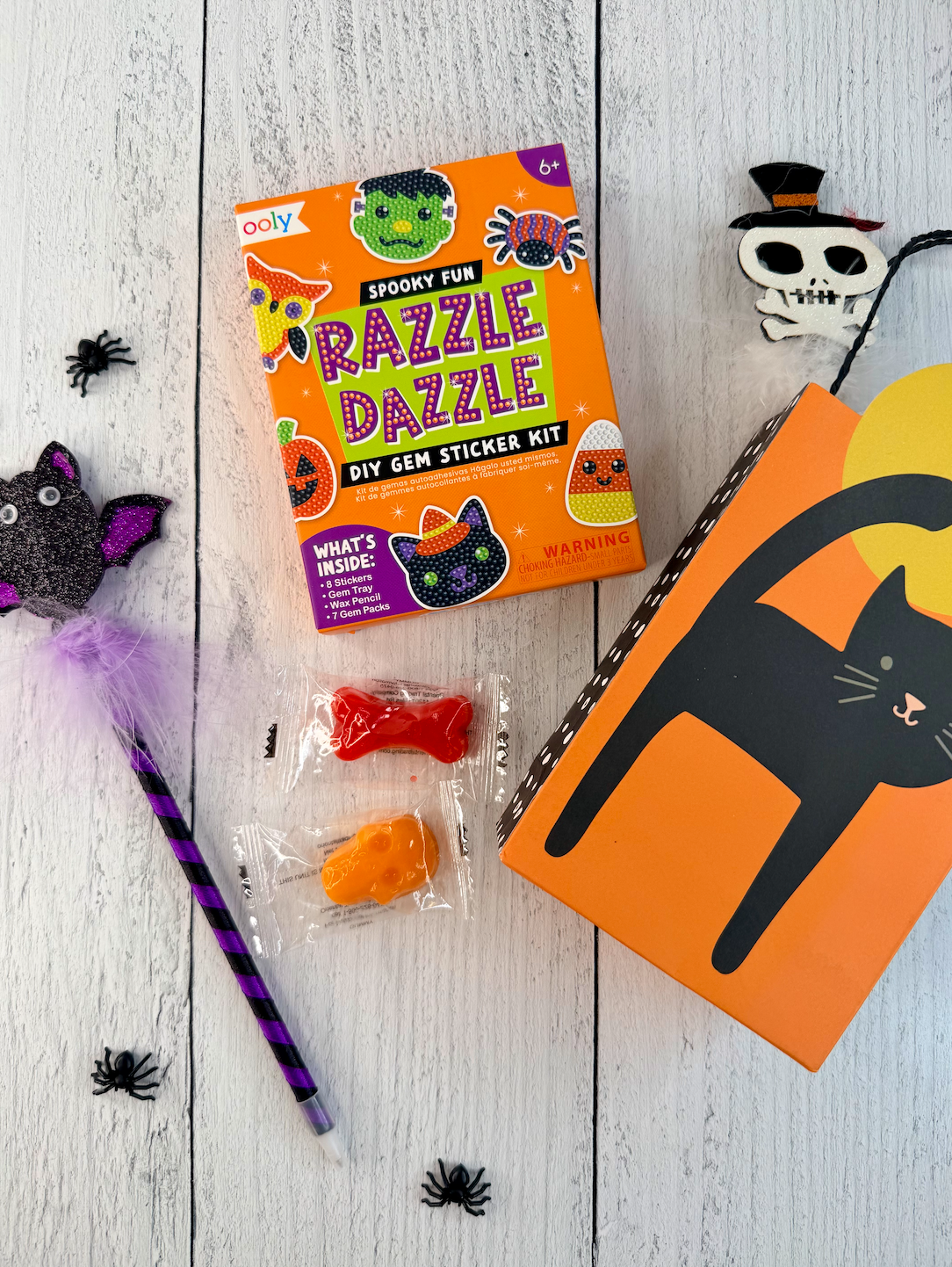 Set of Halloween party favors with gem sticker kits, gummy candy, pencils, and black cat favor boxes.