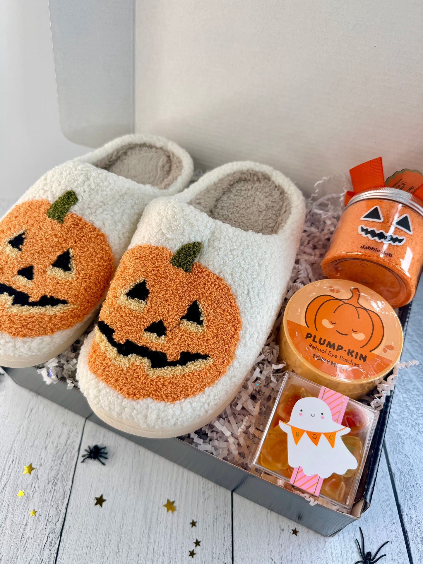 Halloween self-care gift box featuring pumpkin slippers, pumpkin eye patches, seasonal bath product, and a ghost-themed sweet treat