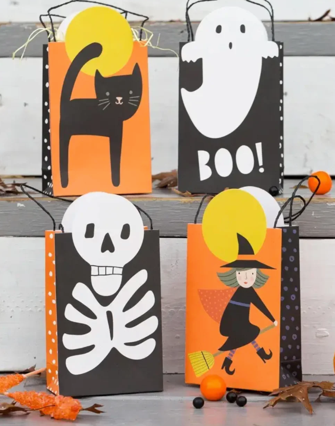 Halloween-themed gift bags with black cat, ghost, skeleton, and witch designs on a wooden surface.
