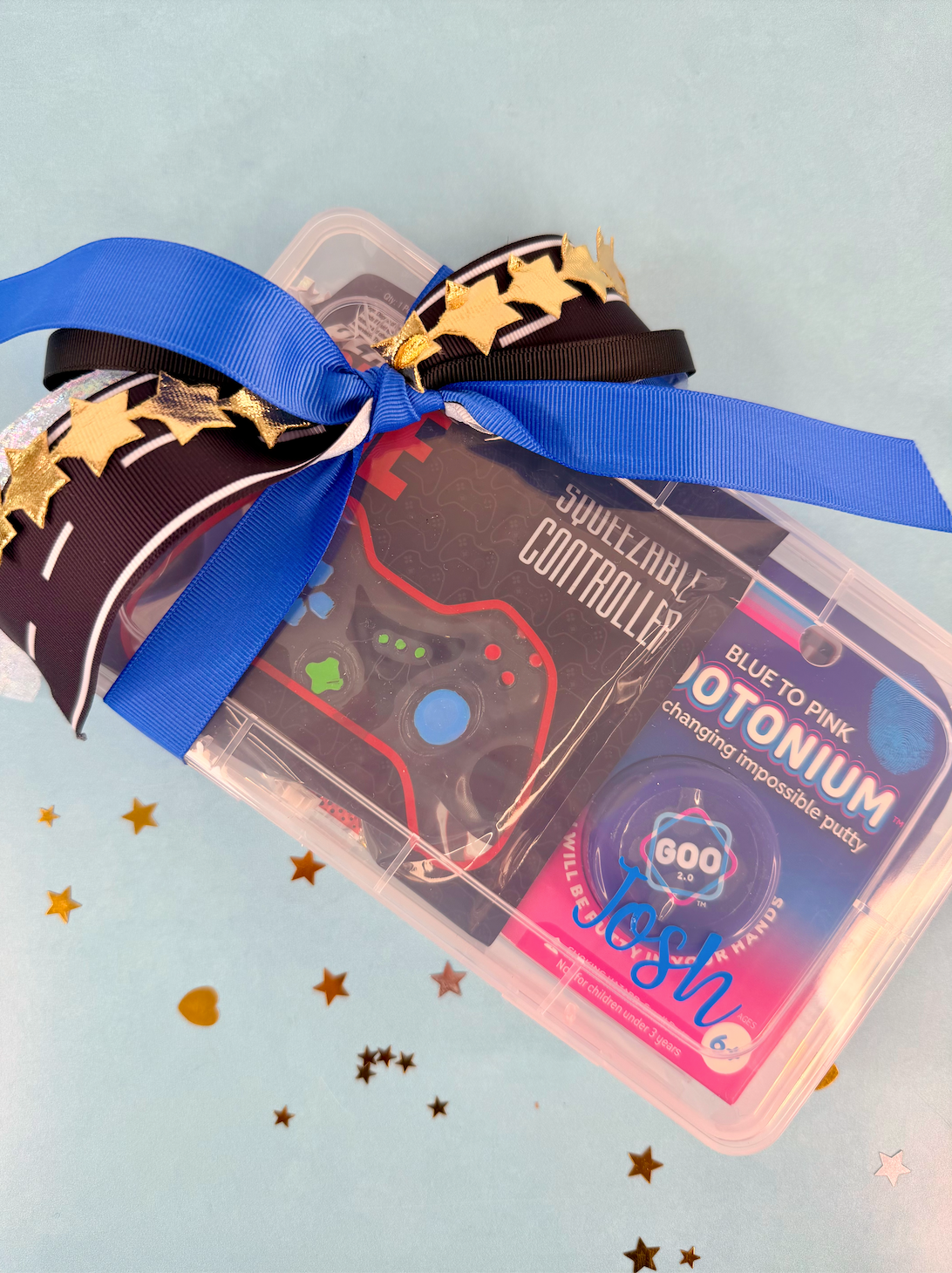 Toy controller with 'Josh' branding, blue ribbon, and star decorations on a light blue background
