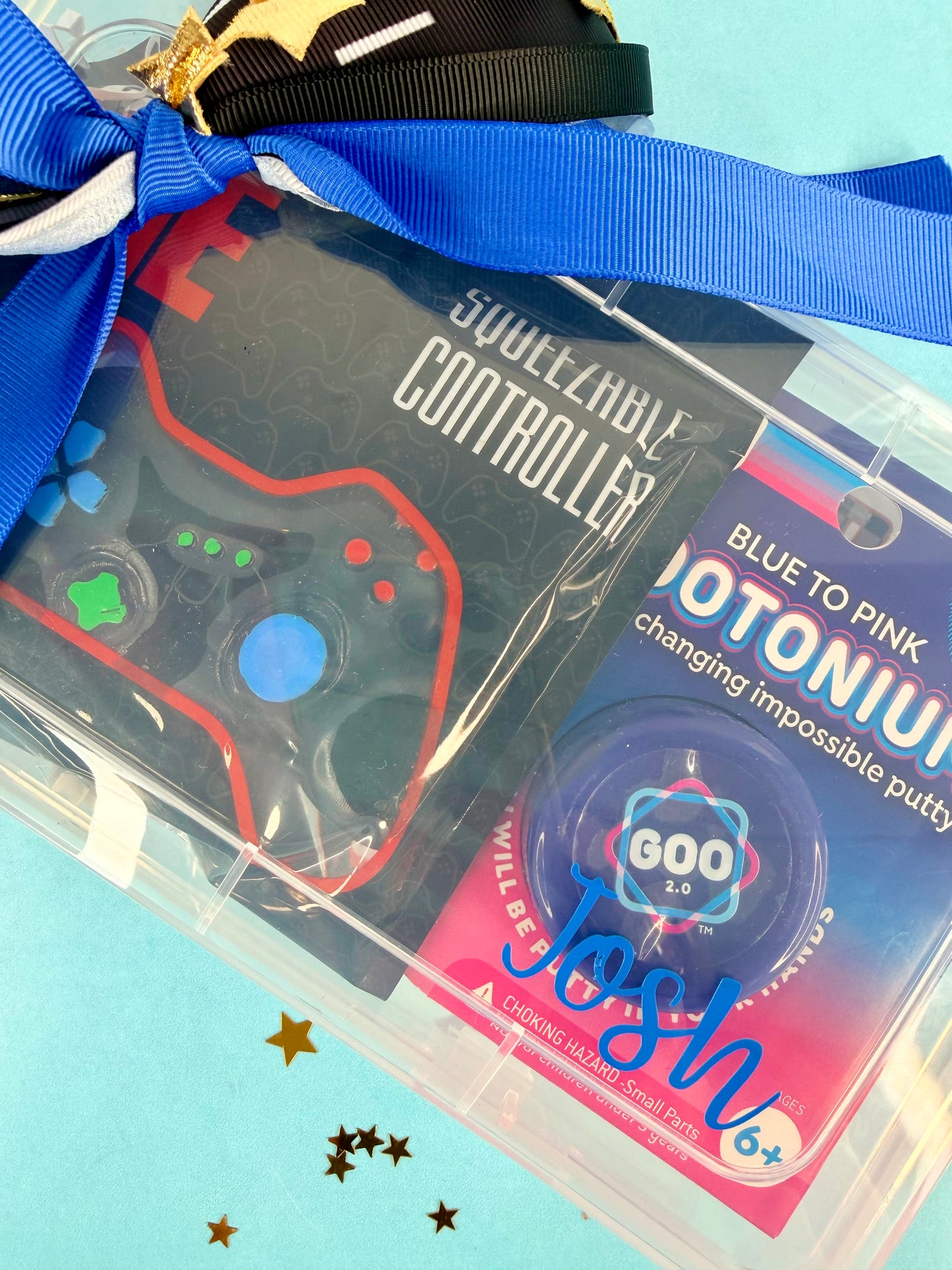 Squeezeable controller toy in clear packaging with blue ribbon on a light blue background