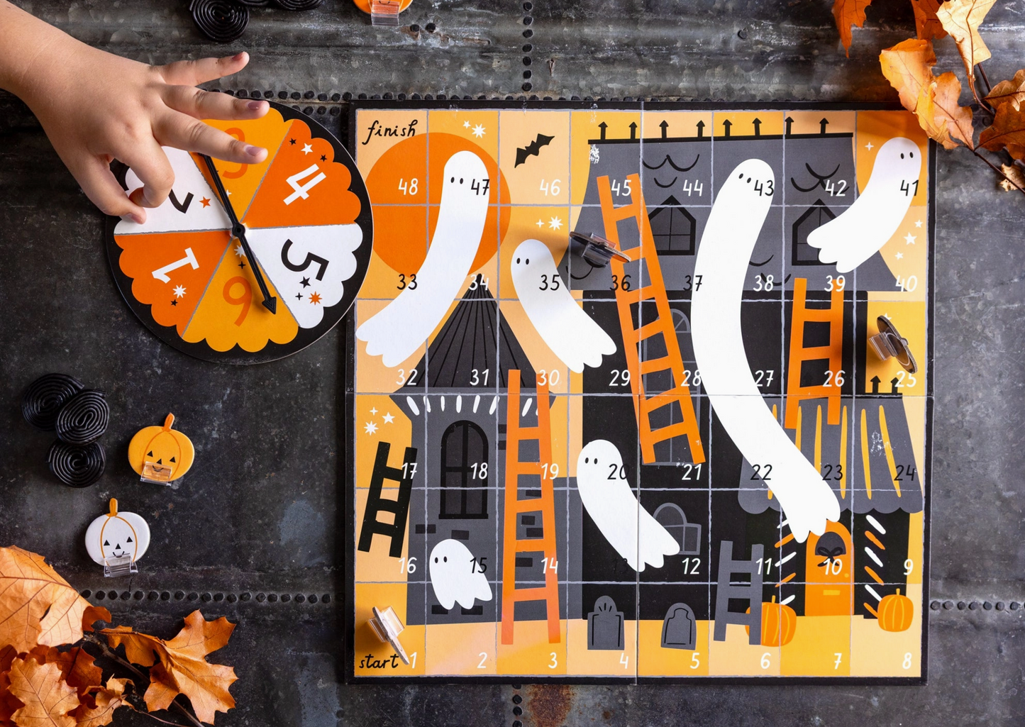 Halloween-themed game board with ghosts, pumpkins, and a ladder on a dark surface.