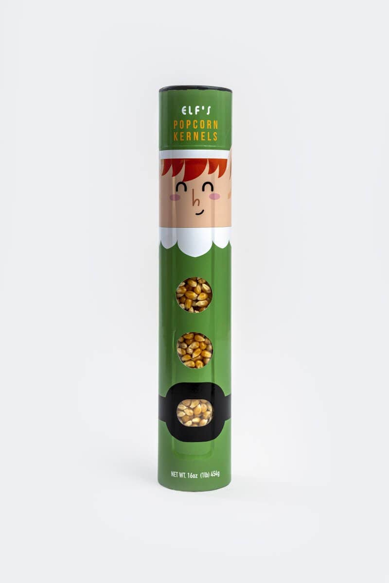 Elf Popcorn Kernels in a green cylindrical container designed like an elf, featuring a cartoon face and three windows showing the golden popcorn kernels inside, set against a plain white background.