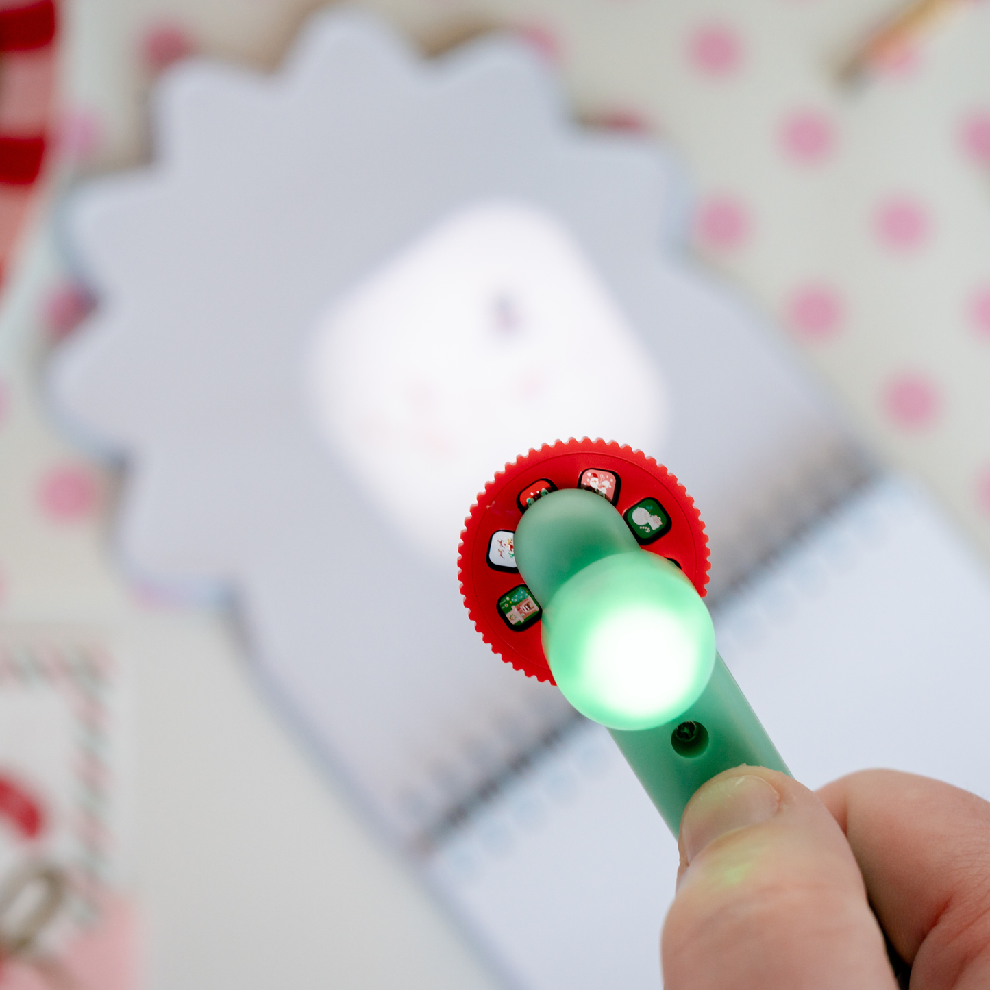 Hand holding a small flashlight with a red and green design against a blurred background