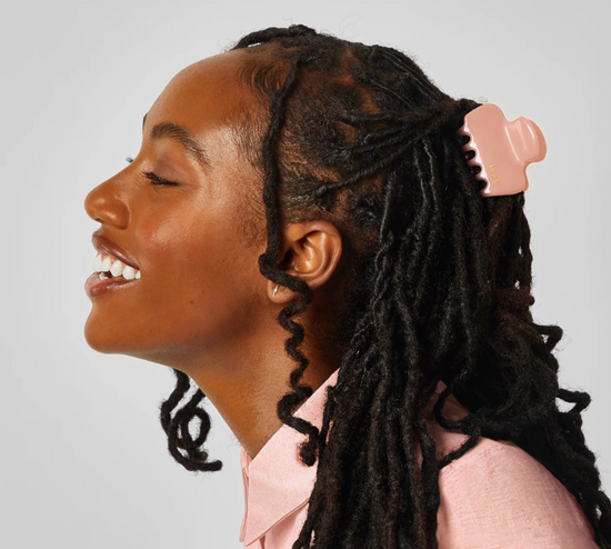 Person with braided hair wearing a pink shirt against a plain background