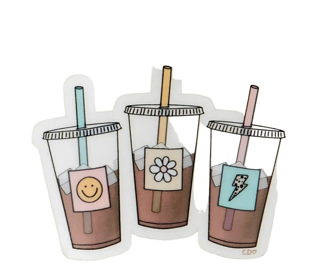 Three die-cut stickers of iced coffee cups with straws, displayed on a soft white textured background. Each cup has a different colored drink and a decorative label: a pink smiley face, a white flower, and a light blue lightning bolt.