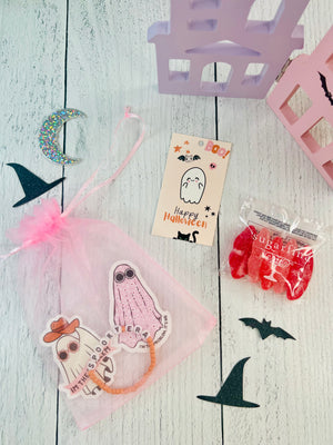 Halloween-themed items including ghost stickers, a card with a ghost, and candy on a wooden surface.