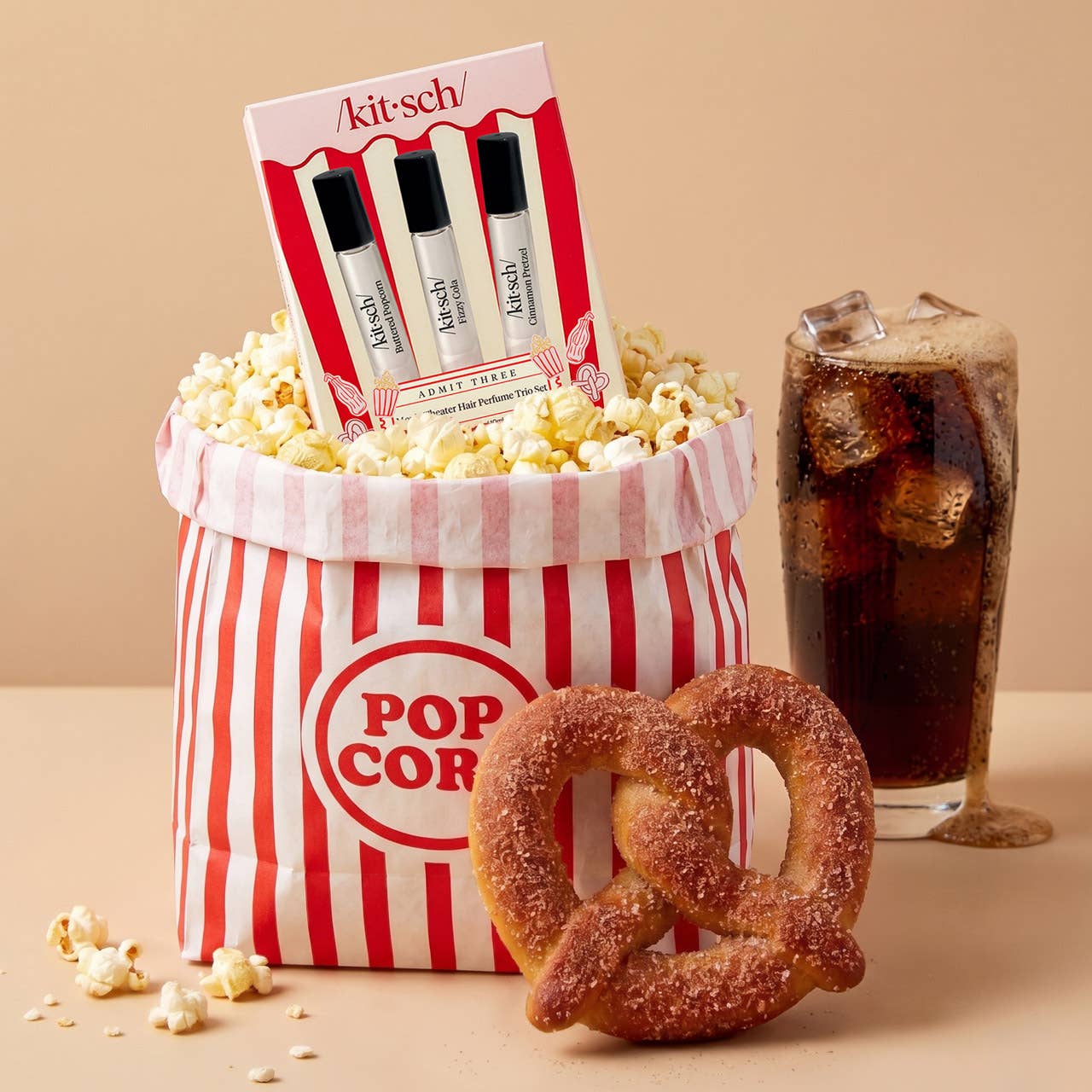 Popcorn bucket with popcorn, a glass of soda, and a pretzel on a beige background