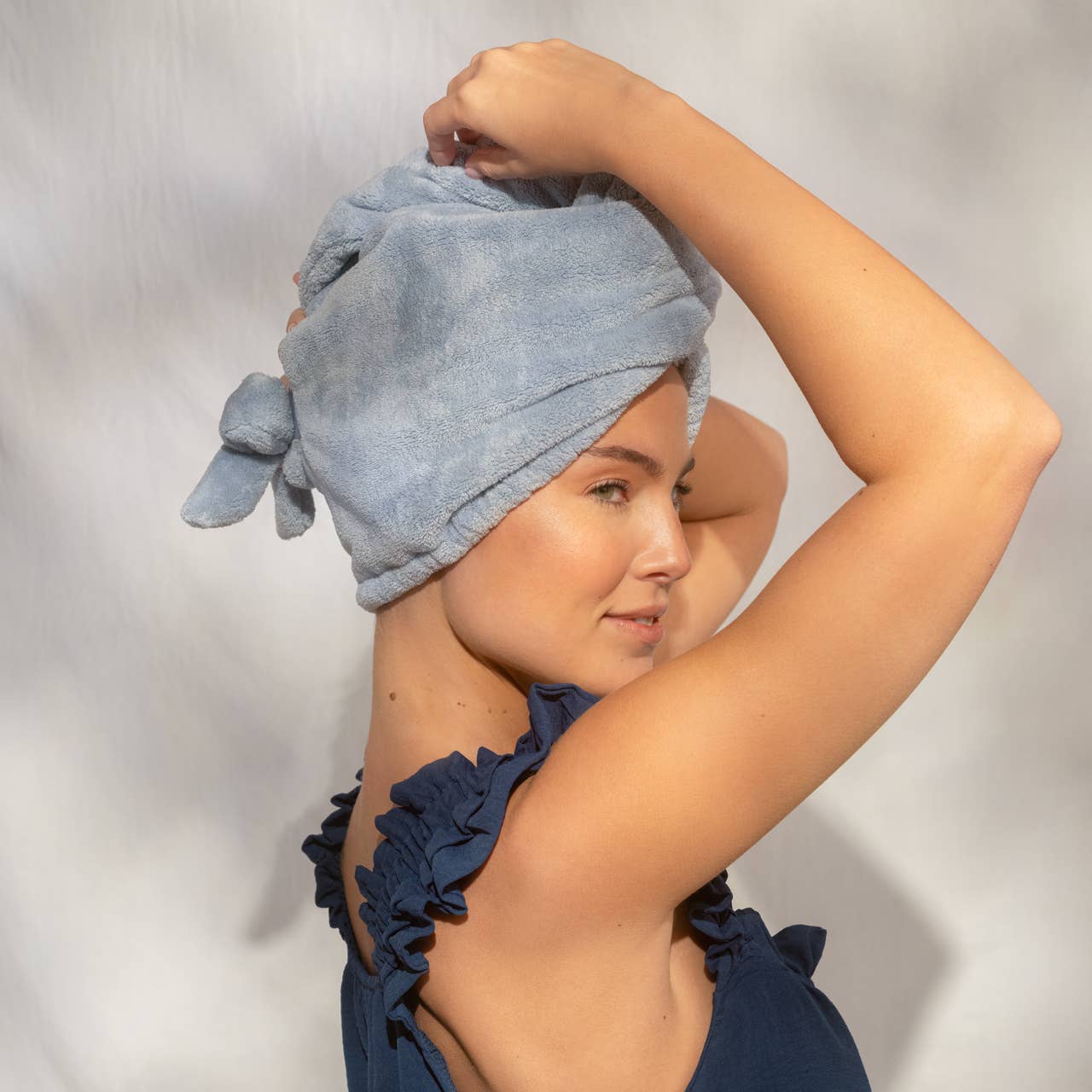 Woman wearing a blue towel on her head against a plain background