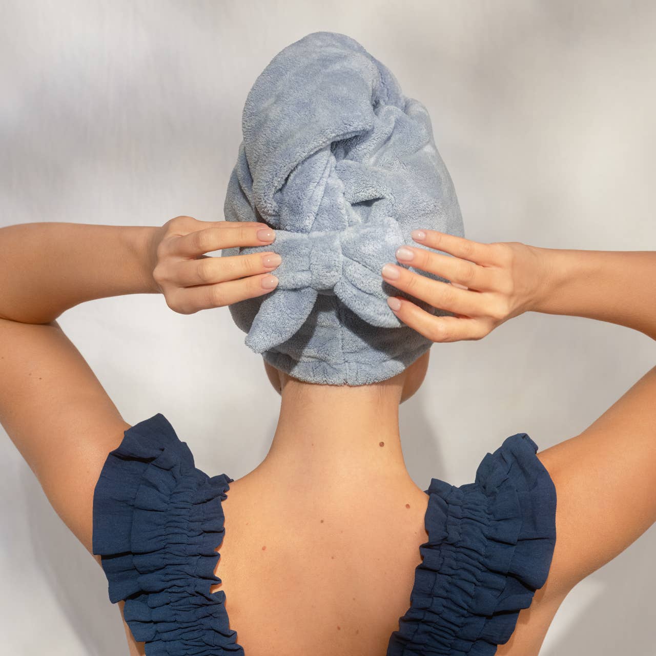 Person using a blue towel to wrap around their head with navy scrunchies on wrists.