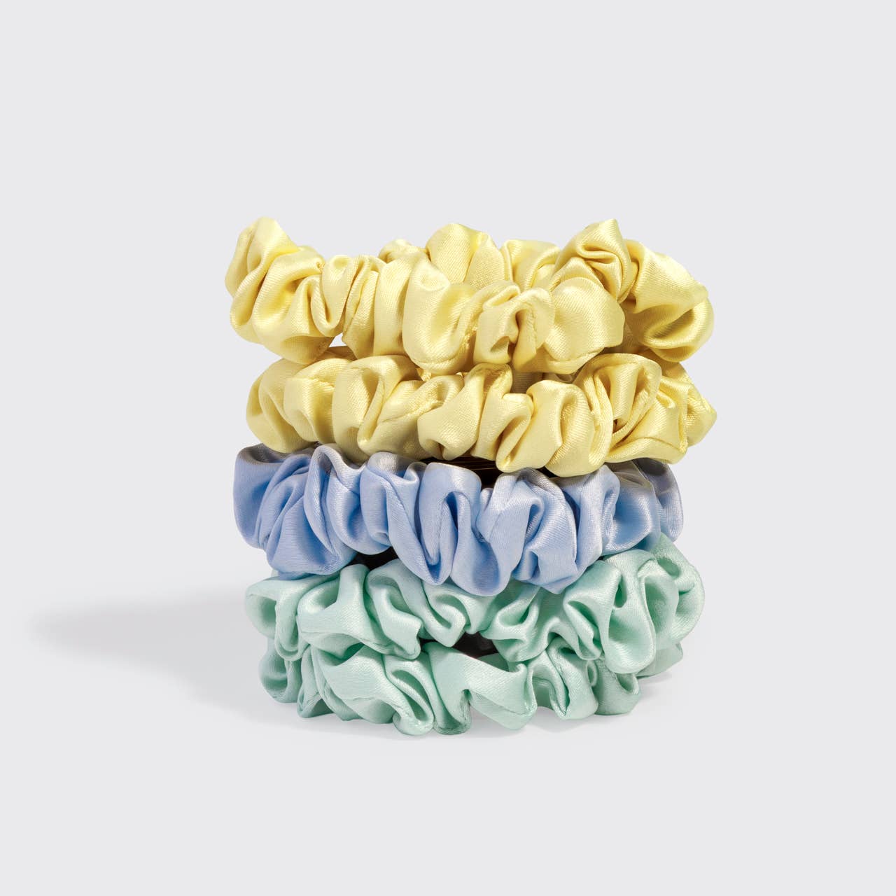 Three scrunchies in yellow, blue, and green on a light gray background