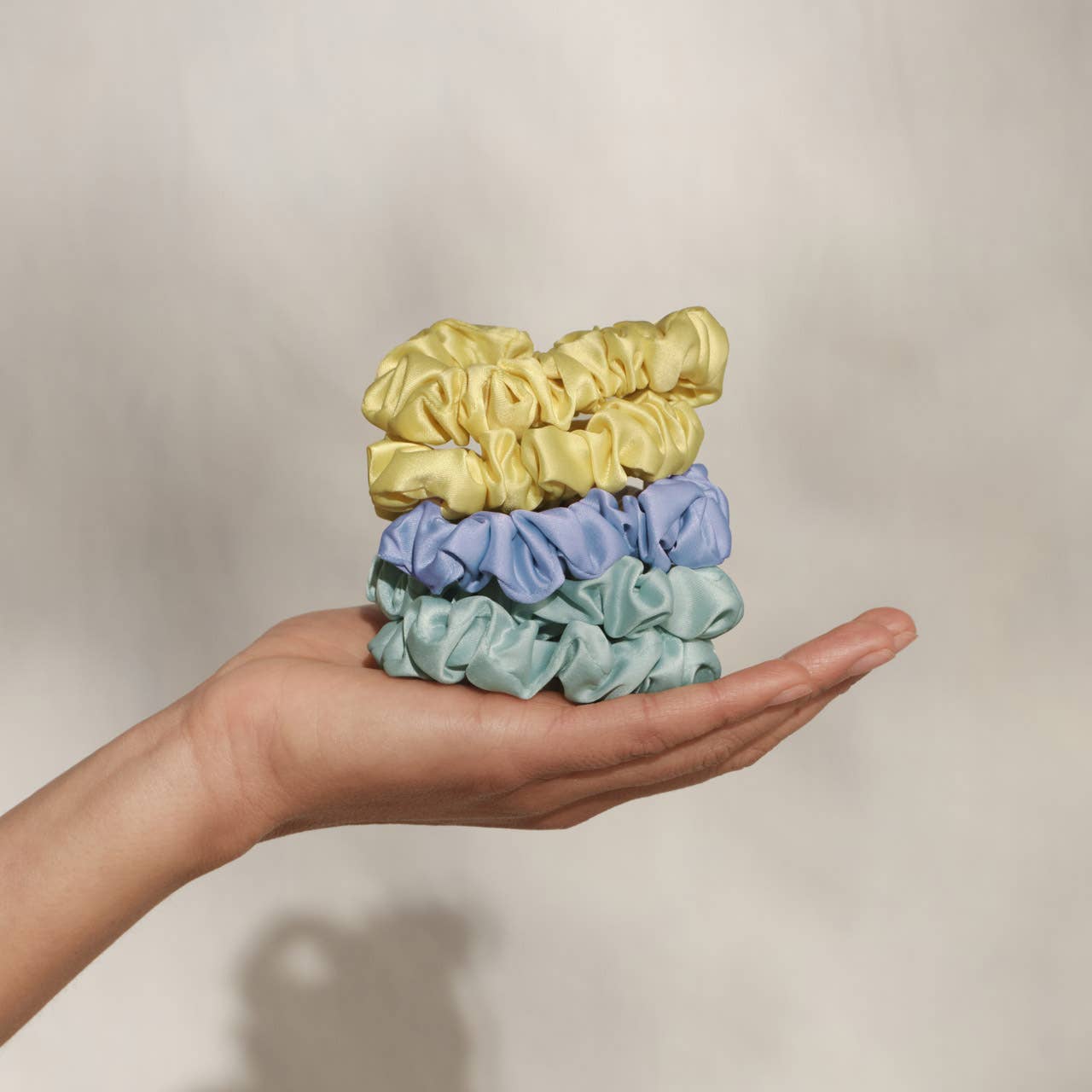 Hand holding three colorful scrunchies against a neutral background