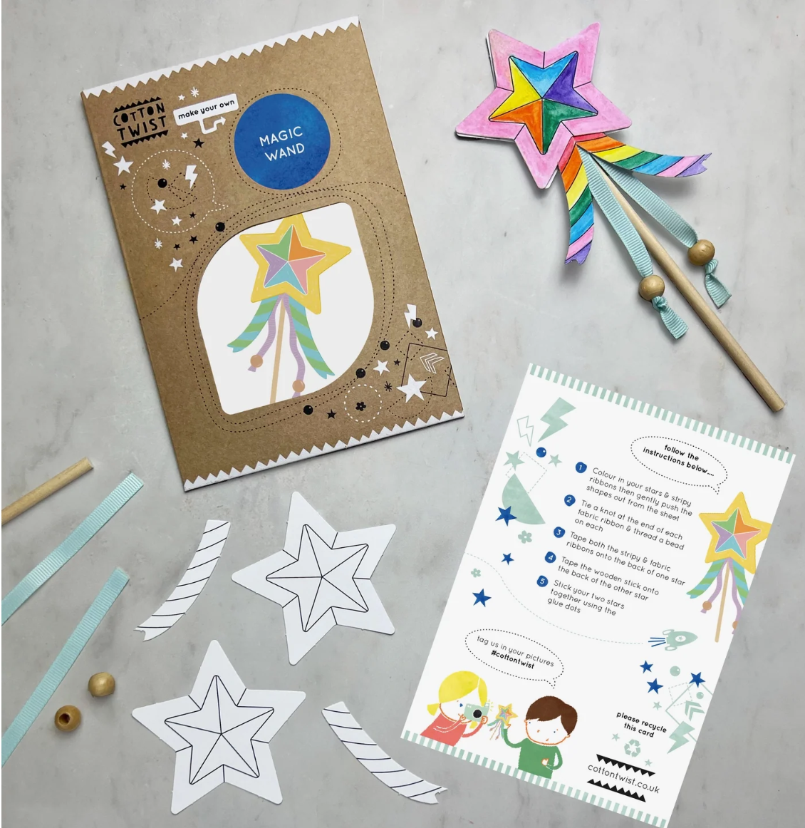 Children's craft kit with star-shaped paper cutouts, a magic wand, and instructions on a gray surface.