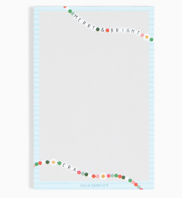 Notepad with 'Merry & Bright' text and colorful border on a light blue background