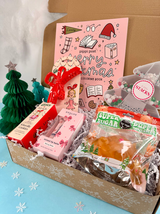 Box of Christmas-themed items including a coloring book, cookies, and candy on a light blue background with snowflake decorations.