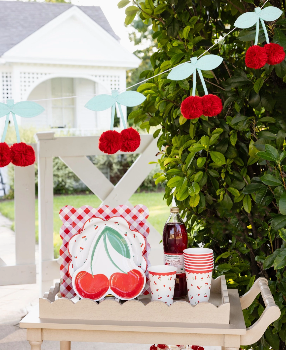 Outdoor setting with cherry-themed decor including a plate, cups, and a bottle on a table.