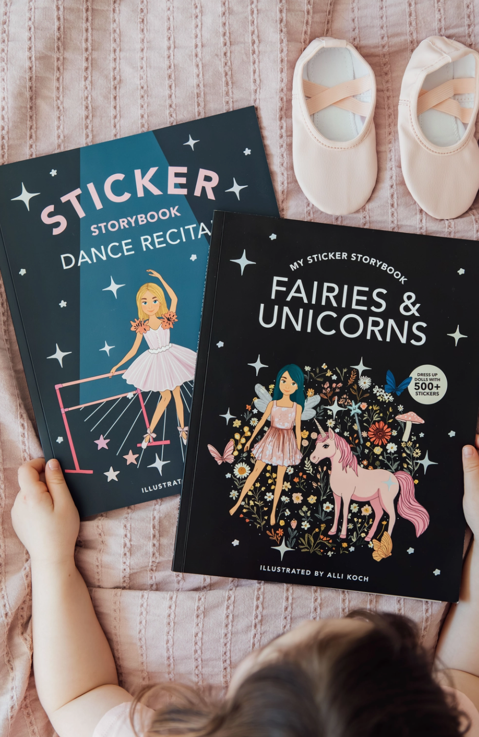 Two children's books titled 'Sticker Storybook Dance Recital' and 'My Sticker Storybook Fairies & Unicorns' on a bed.