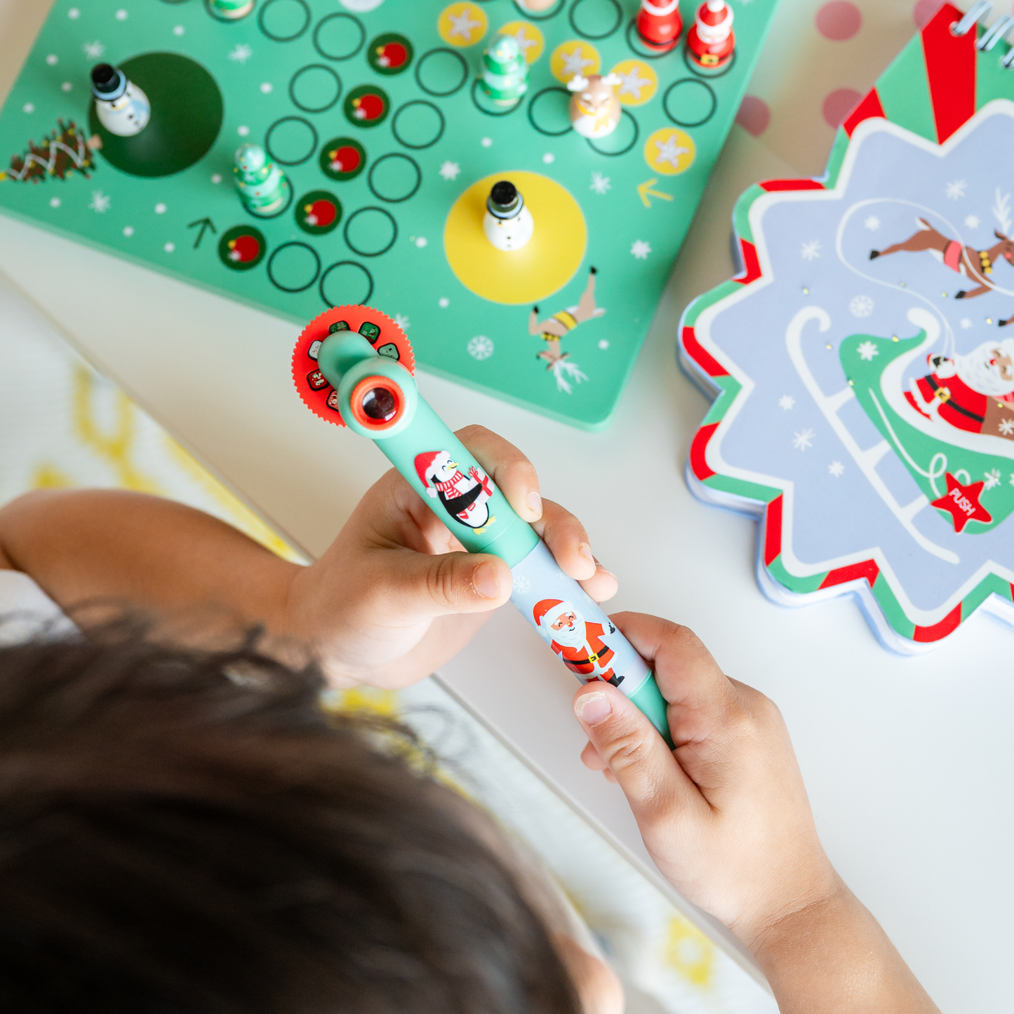 Child playing with a Christmas-themed toy on a table with a board game and festive decorations.