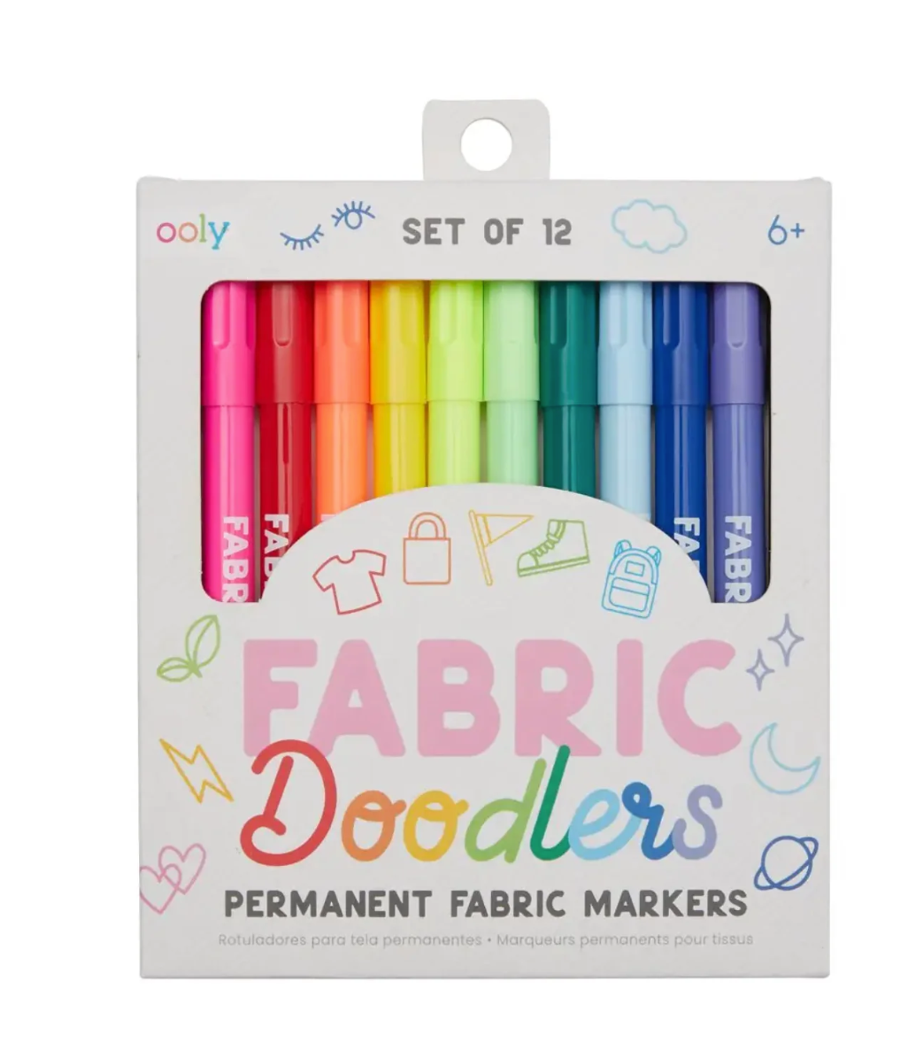 A 12-pack set of colorful fabric markers in a white cardboard box with a clear window. The markers are arranged in a rainbow sequence from pink and red to green, blue, and purple.