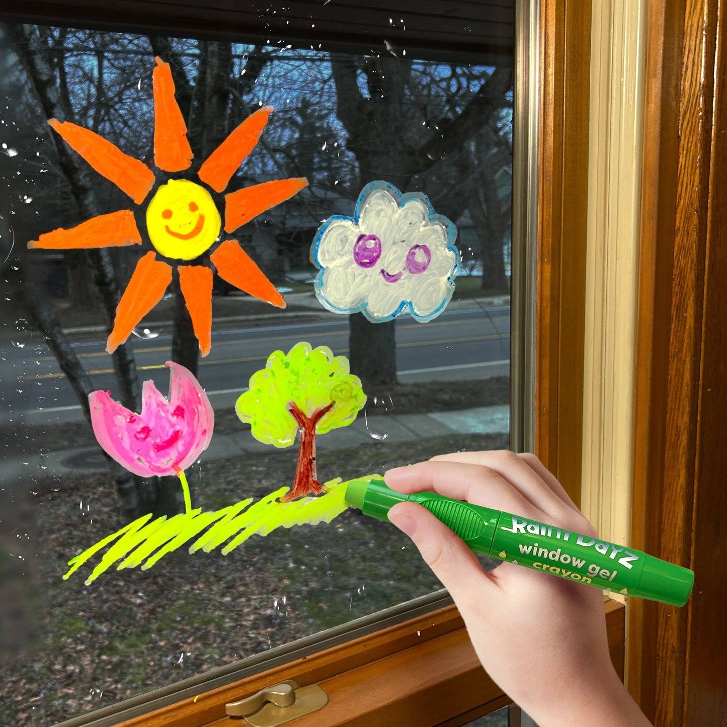 Hand holding a green window gel crayon with colorful window decorations on a glass door.