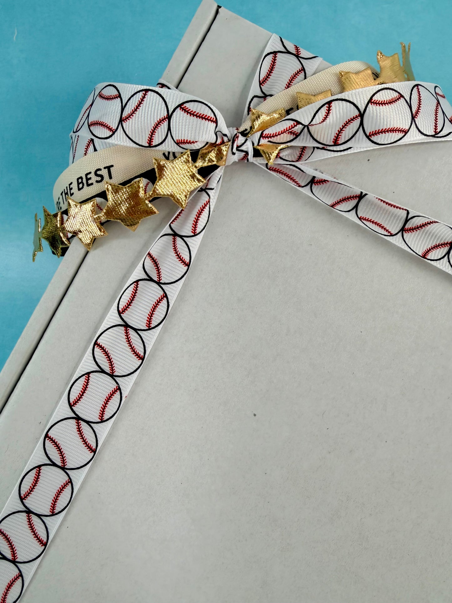 Decorative ribbon with baseball pattern and gold accents on a white surface.