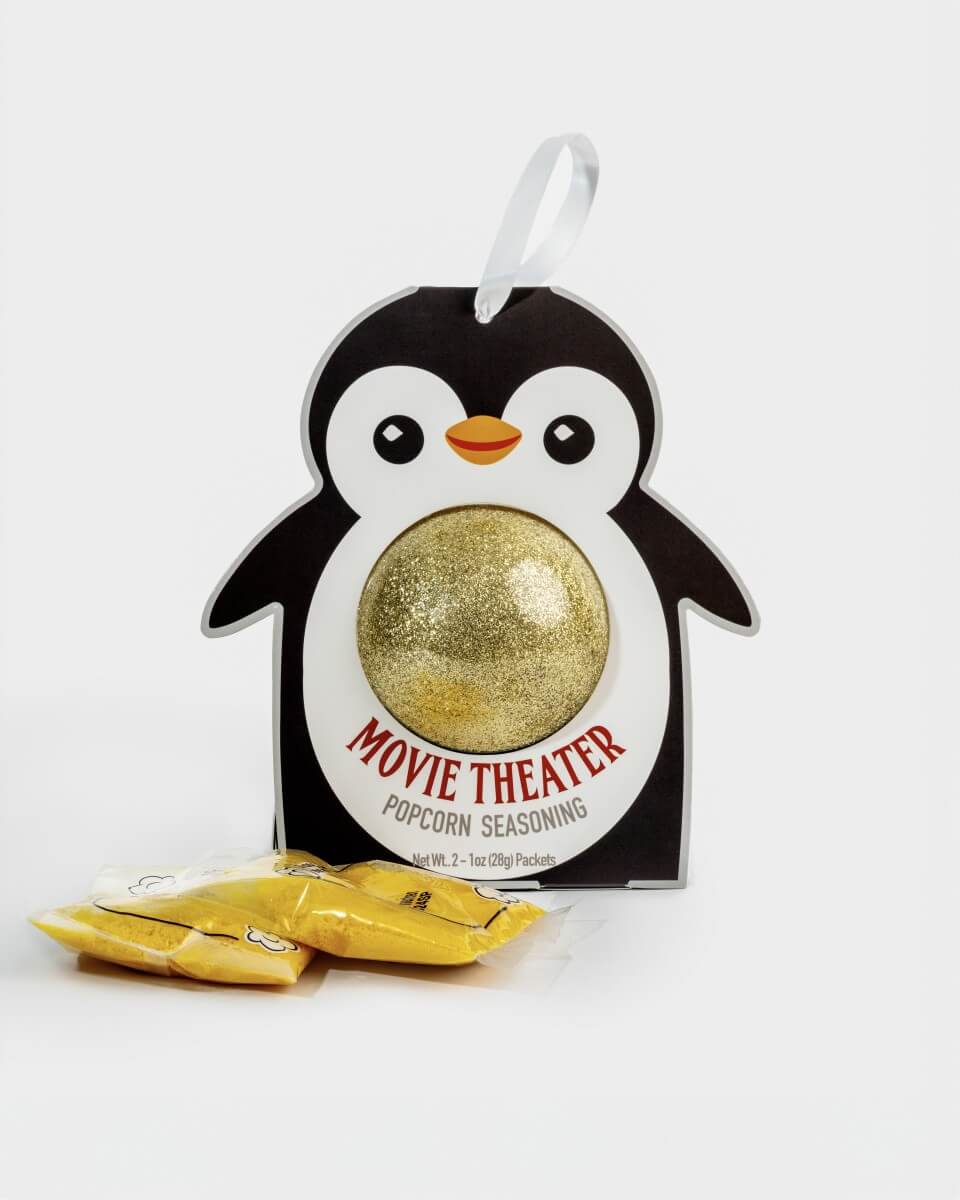 A penguin-shaped package of Movie Theater Popcorn Seasoning with a gold glitter ball visible in the center and two small yellow seasoning packets placed in front on a white background.